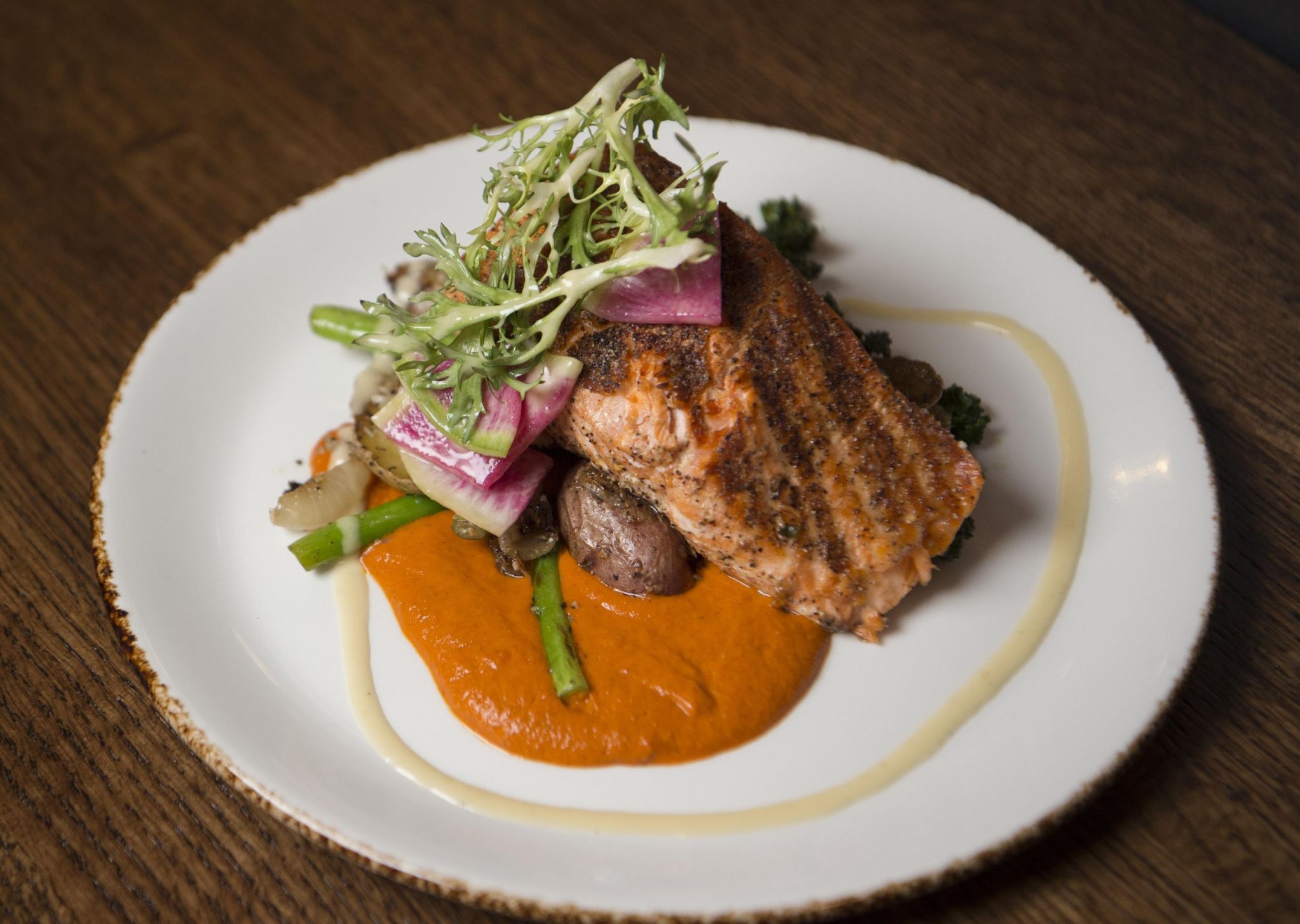 Grilled salmon with a garnish of watermelon radish and frisse, atop a bed of roasted potatoes and asparagus with an orange sauce from the Steam Plant Restaurant